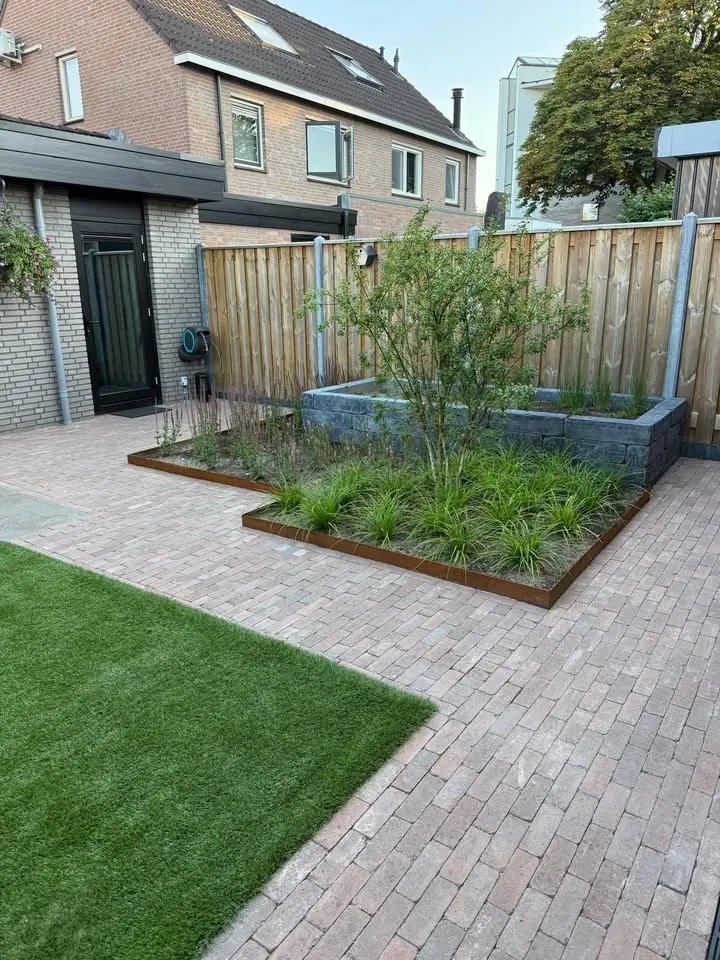 Achtertuin met paden van gebakken klinkers, borders met een rand van cortenstaal, een verhoogde border en kunstgras