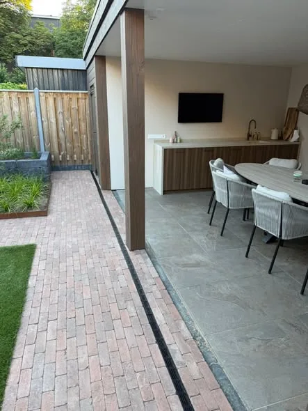 Pad van gebakken klinkers met een lijngoot langs het terras onder de overkapping