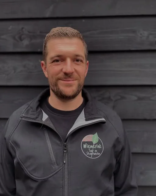Mick Wiemerink in een zwarte werkjas met het logo van Wiemerink Tuin- en Straatwerken